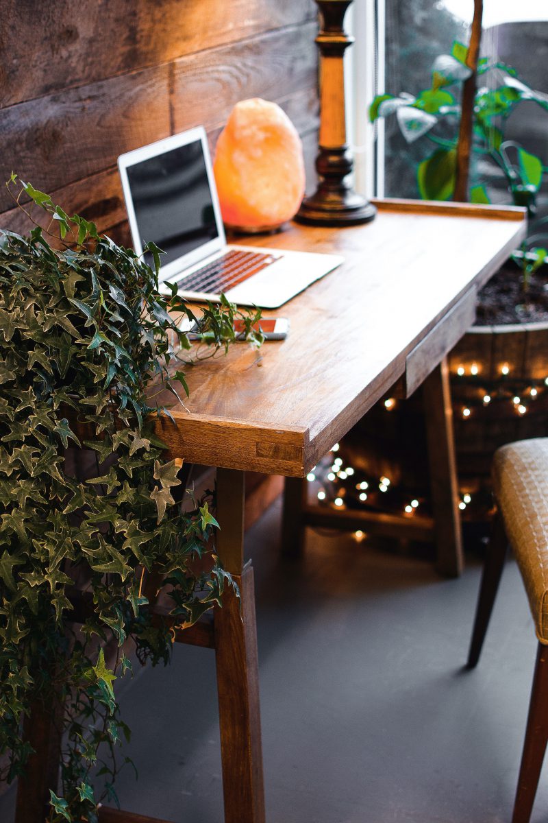 a wood desk with laptop and salt lamp and plant