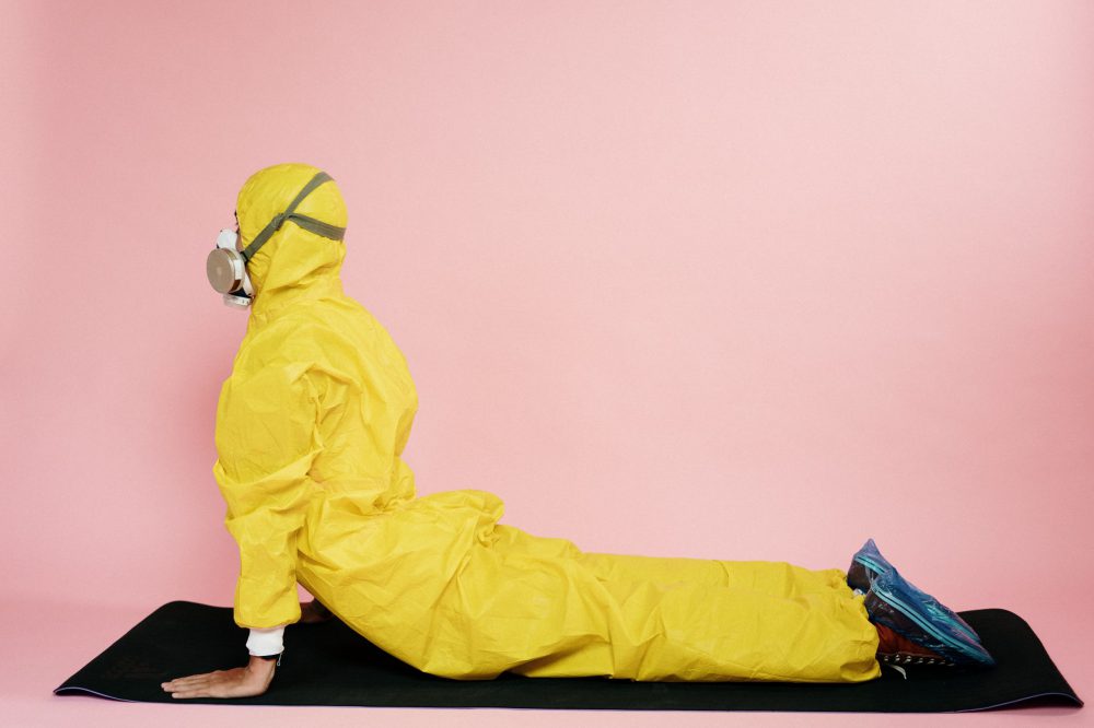 man in yellow protective suit stretching on yoga mat in quarantine